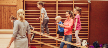 Kinder klettern mit Hilfe Ihrer Eltern auf eine schräg gestellte Langbank.